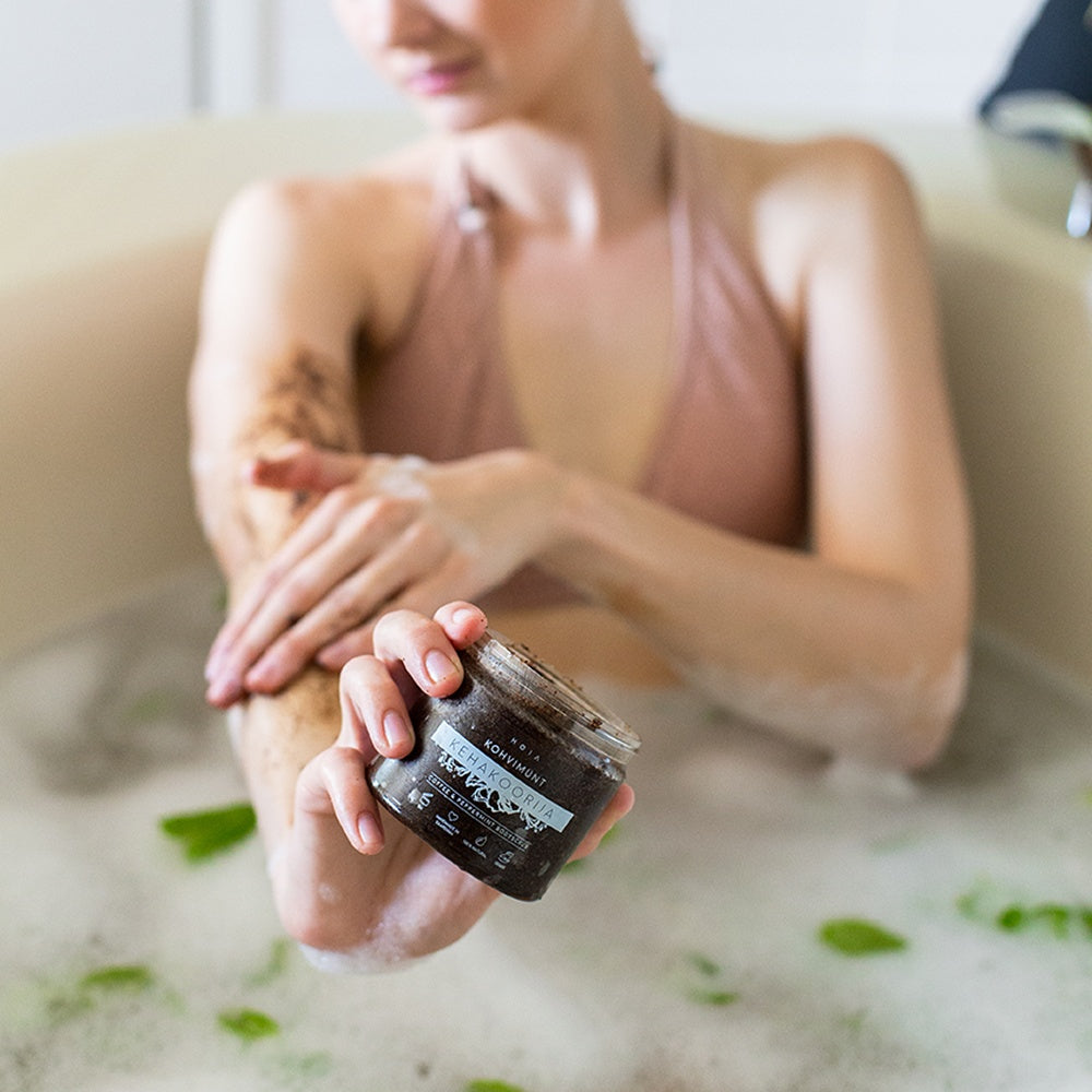 Person in a bathtub holding HOIA Coffee & Peppermint Body Scrub