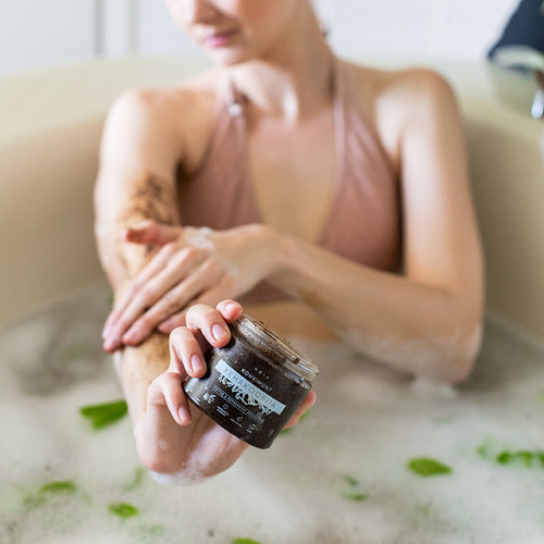Person in a bathtub holding HOIA Coffee & Peppermint Body Scrub