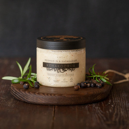 HOIA Rosemary & Juniper Body Scrub on a wooden board with herbs and berries on a dark background